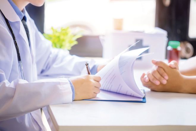 A doctor writing notes during a consultation with a patient.