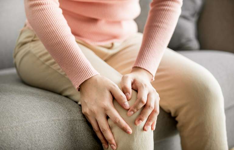 Person sitting on a couch, holding their knee in discomfort