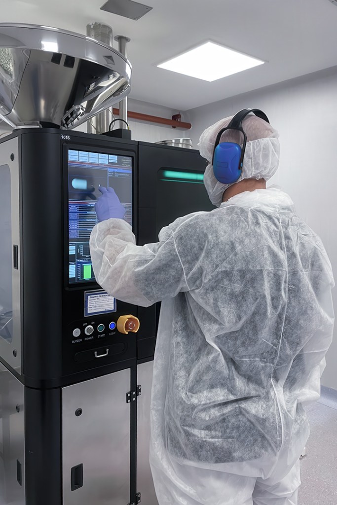 Person in protective gear operating a touchscreen machine in a cleanroom