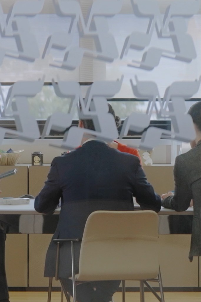 View of a meeting room with people seated at a table, partially obscured by glass.