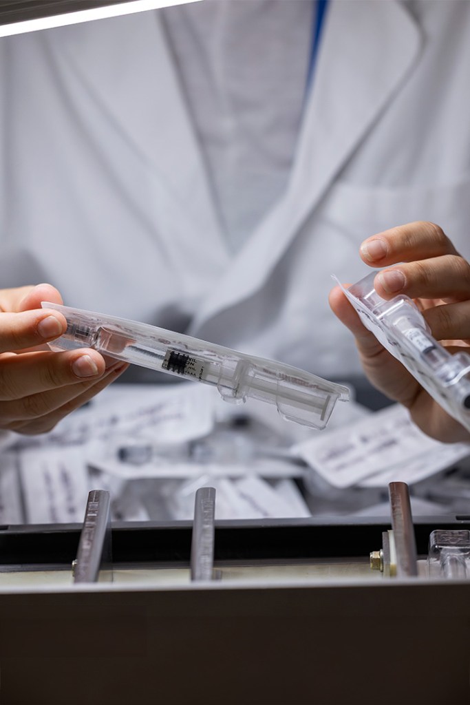 Hands holding a syringe in a medical setting with labels in the background.