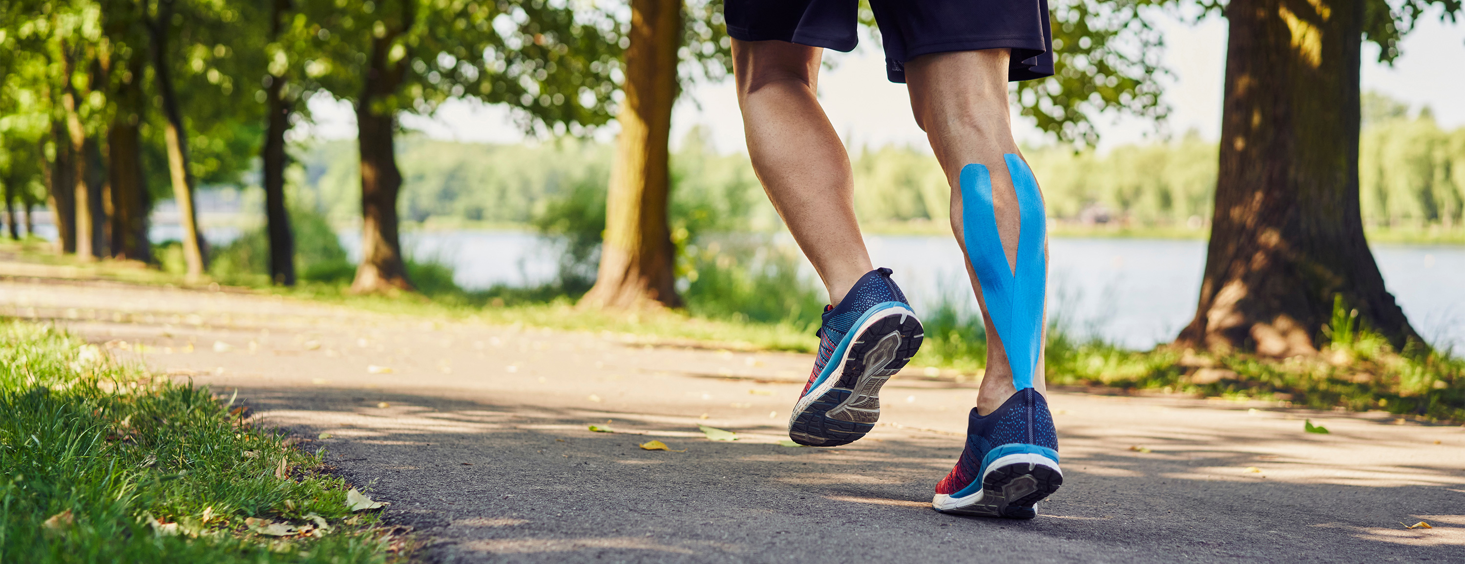 Person jogging on a path with blue kinesiology tape on their calf