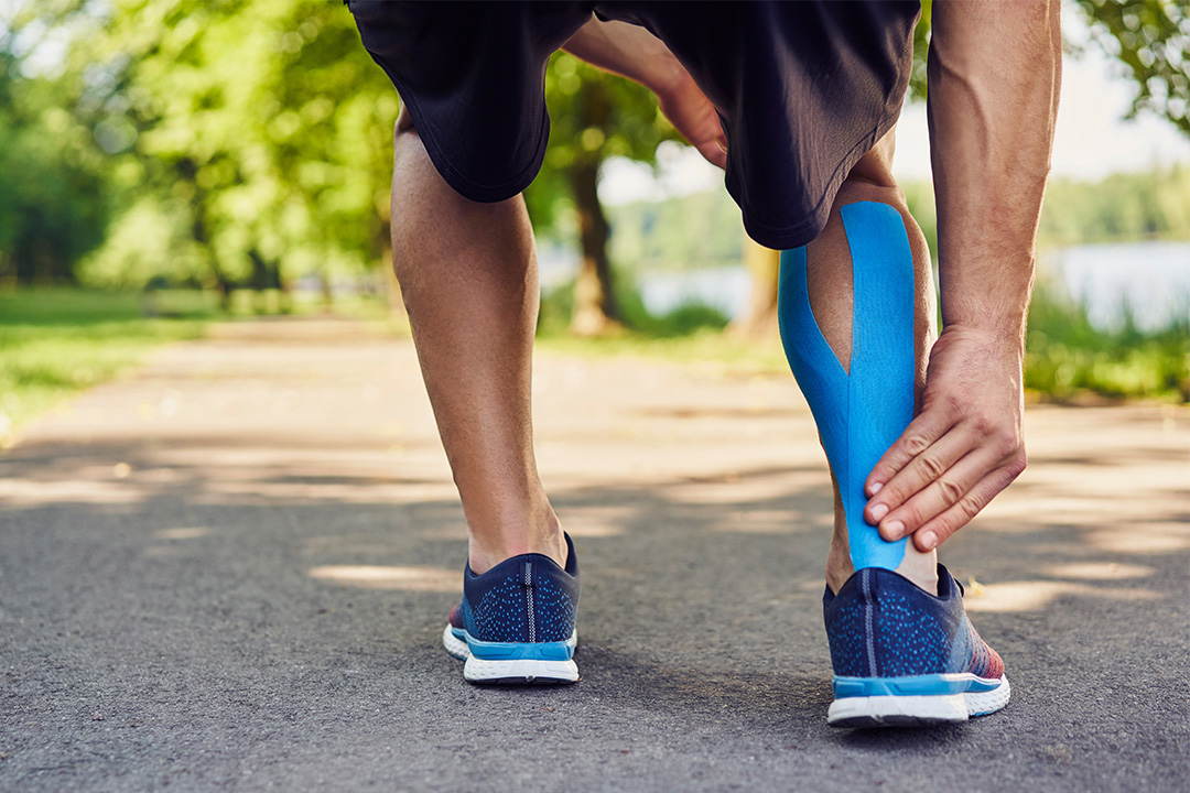 Person applying kinesiology tape to their calf while walking on a path