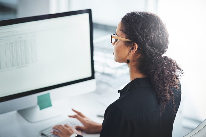 Woman with curly hair working on a computer, viewing a spreadsheet.